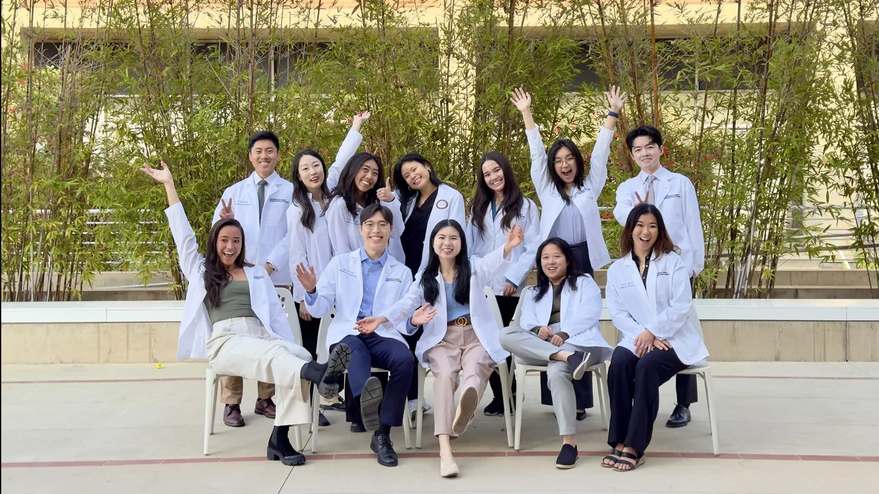 The Asian Pacific American Medical Student Association  in white lab coats standing together, smiling for a photo in a clinical environment.